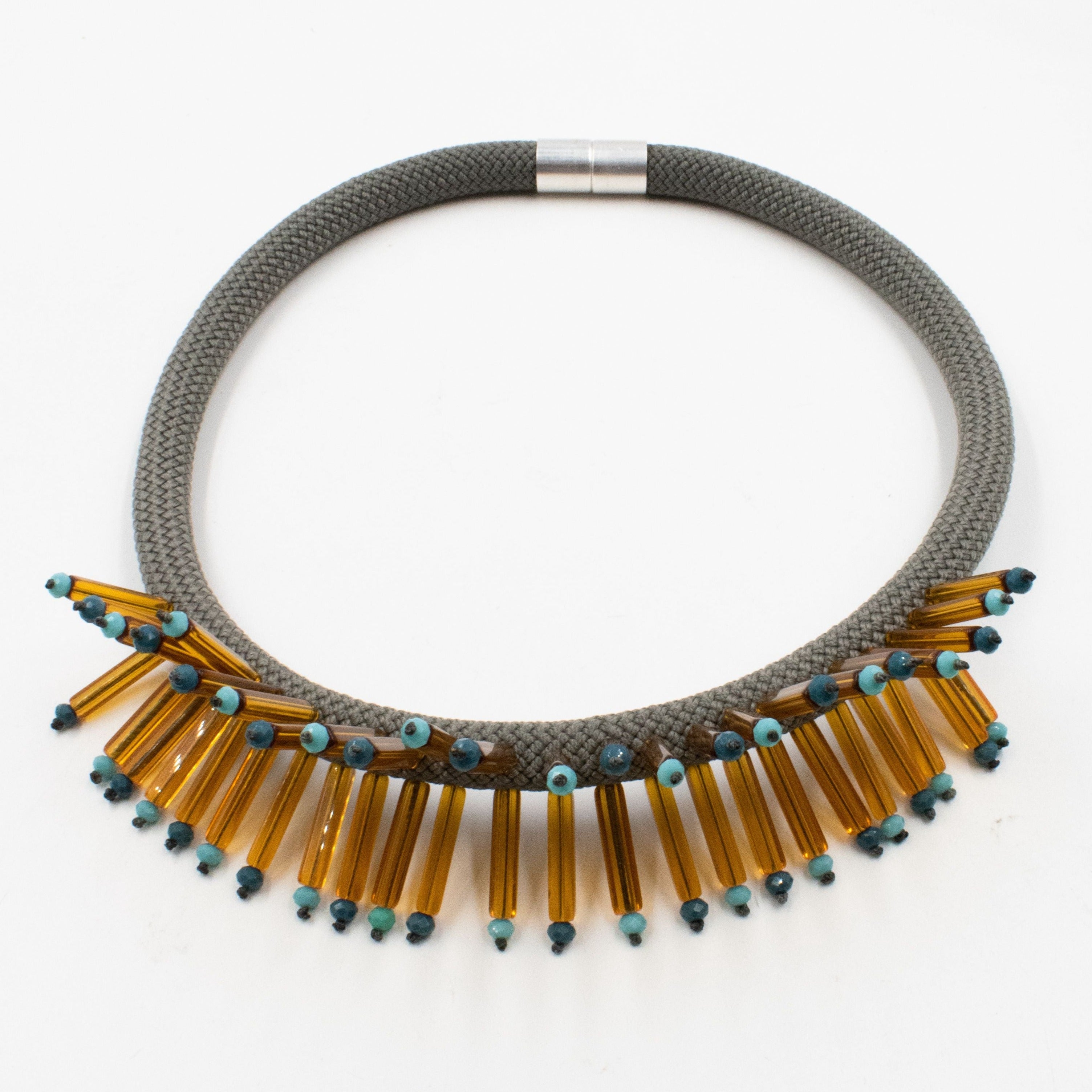 Gray rope necklace with amber glass and teal bead accents.  The amber pieces are arranged in a fringe at the bottom.