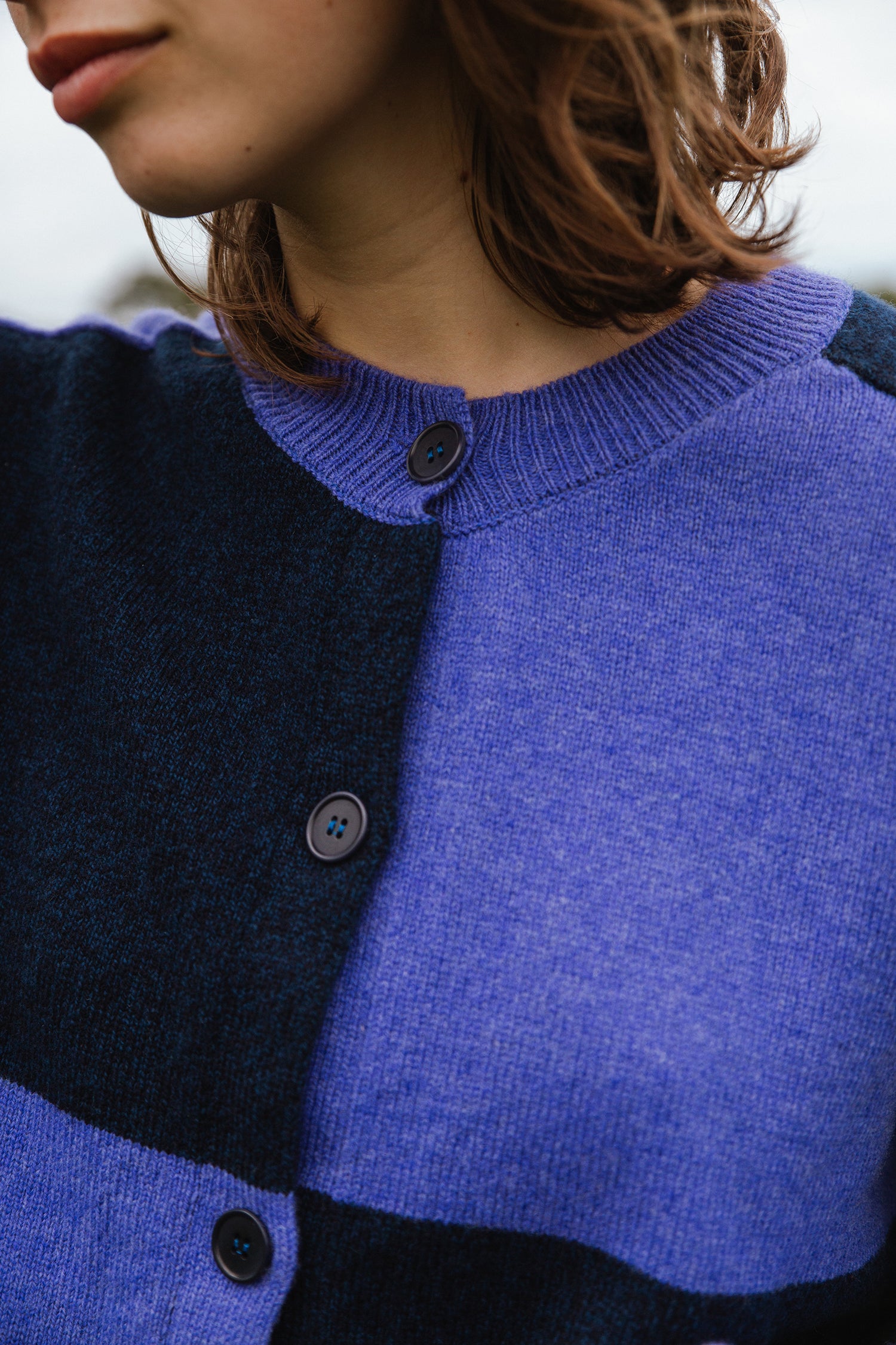Close-up of a blue and dark-blue color-blocked knit cardigan with dark buttons.
