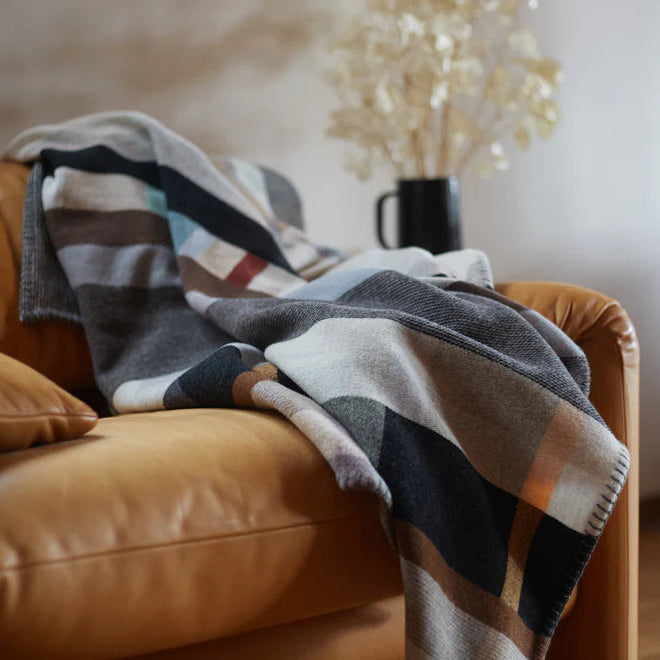 Plaid blanket draped over a brown leather chair with a blurred indoor background