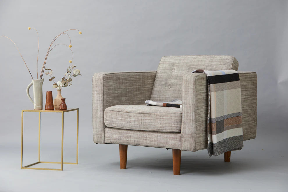 Gray armchair with a patterned throw blanket next to a small gold side table with decorative items on a gray background