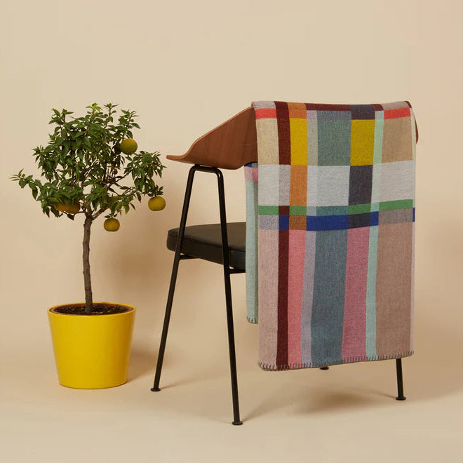 Chair with a colorful geometric-patterned blanket draped over it, next to a potted plant on a beige background