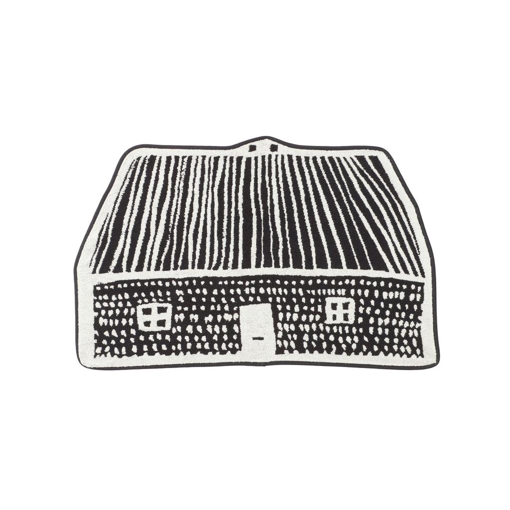 A black and white rug shaped like a house by Donna Wilson, featuring a roof with stripes and a door.