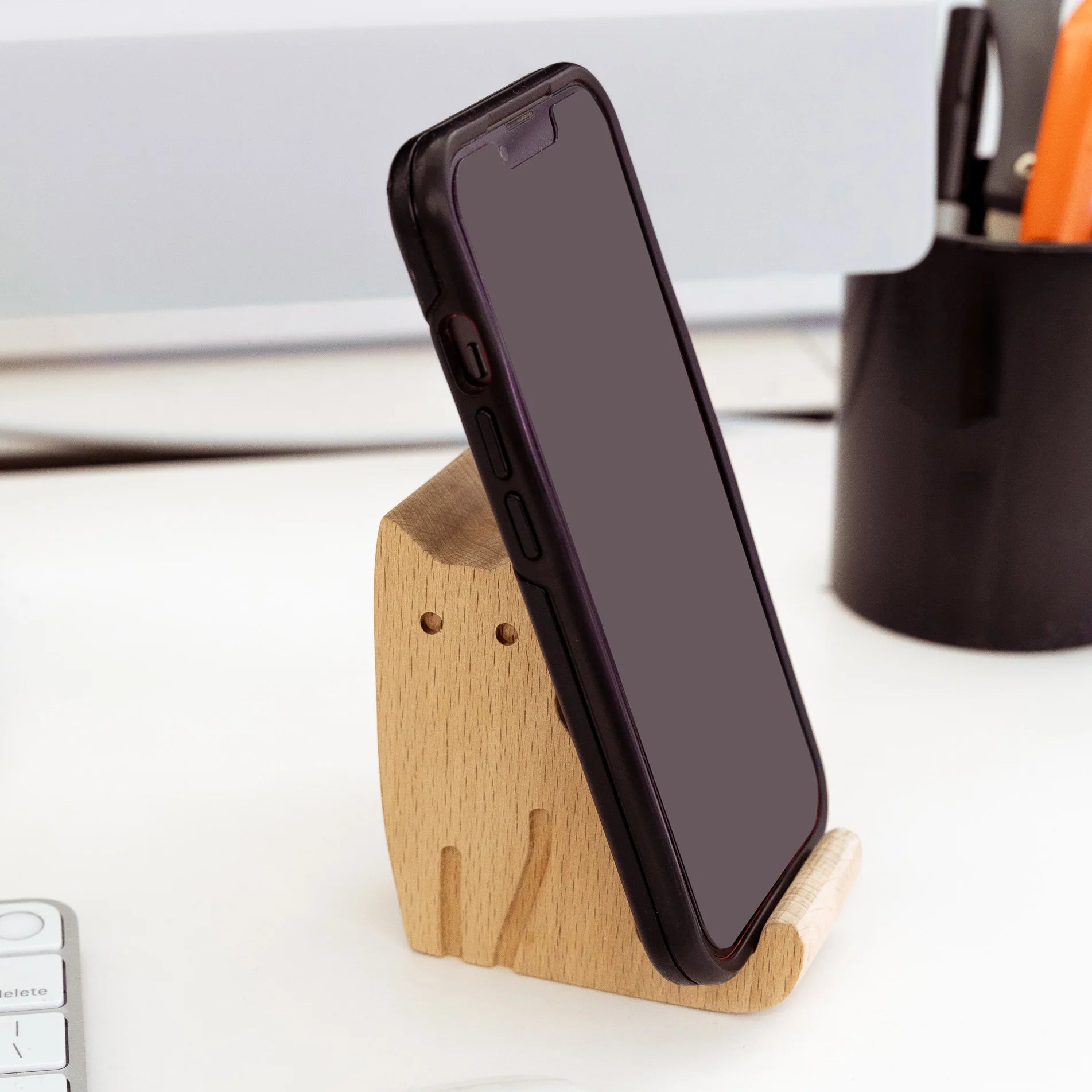 Smartphone in a light brown wooden cat-shaped stand. The phone has a dark case and blank screen.