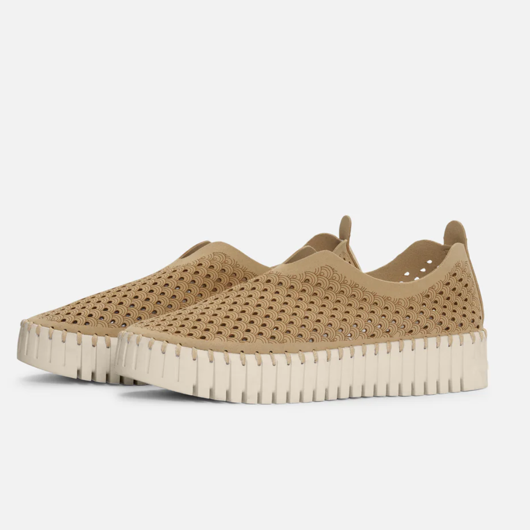 Tan slip-on shoes with a cream-colored, scalloped sole and a repeating wave-like perforated pattern.