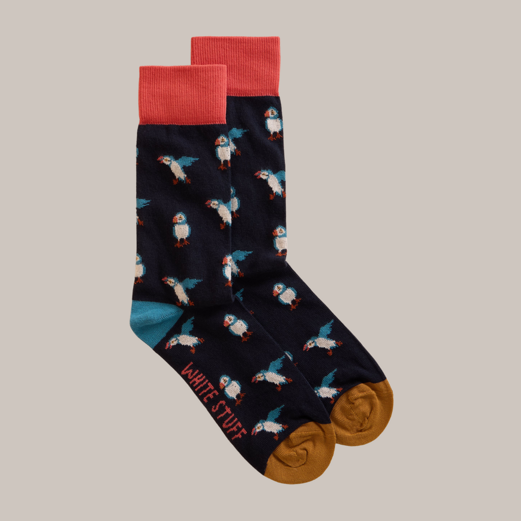 Pair of dark navy blue socks with a repeating puffin pattern, coral-colored cuffs, and mustard-yellow heels and toes.