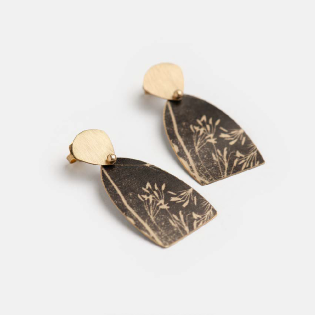 Pair of dark, arched earrings with gold accents and a botanical print.