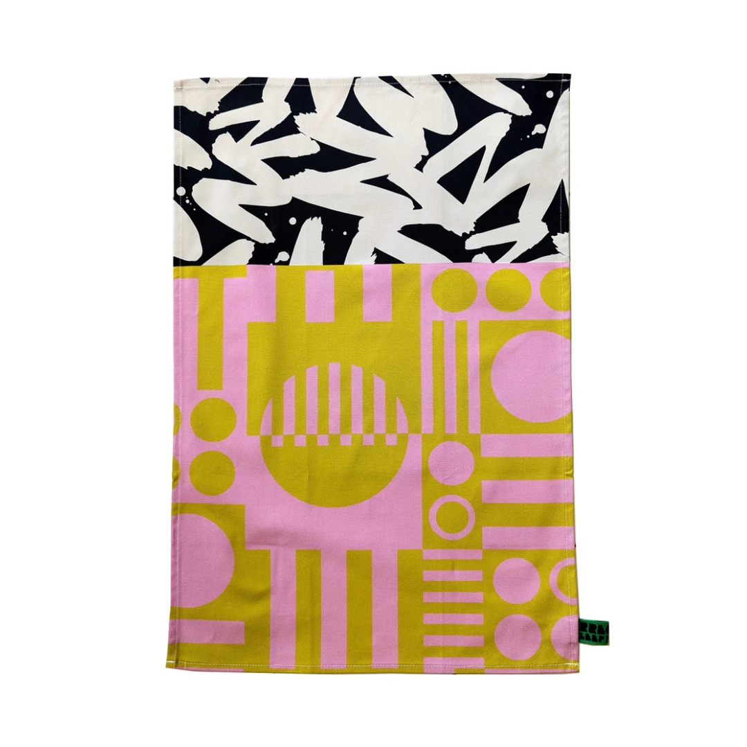 Abstract geometric and brushstroke patterned tea towel in pink, gold, black, and white.