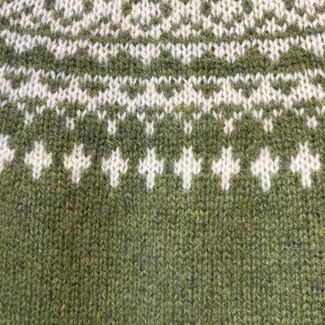 Close-up of olive green wool knit fabric with a Fair Isle-style pattern in off-white.