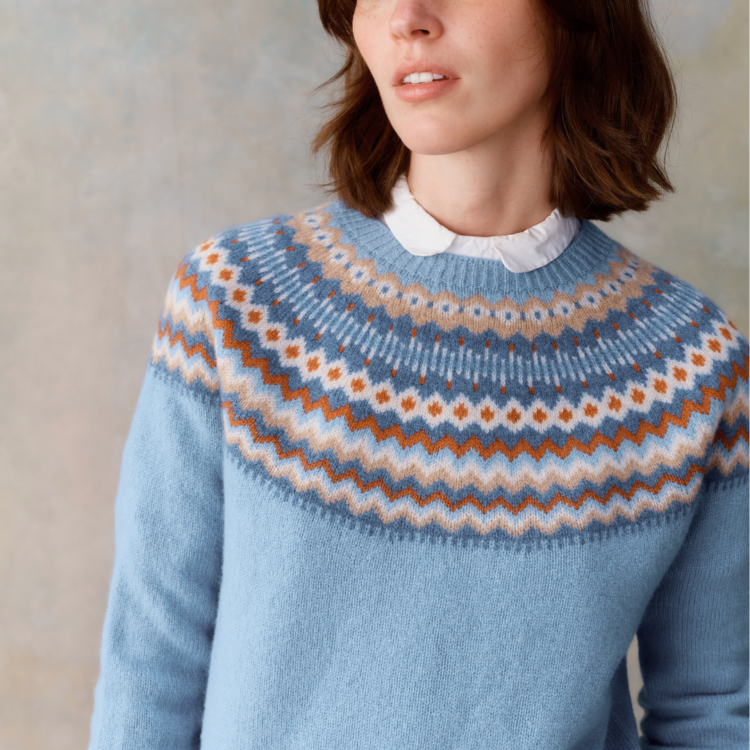 Light blue crewneck sweater with a Fair Isle-style yoke featuring a repeating pattern in orange, beige, and white.