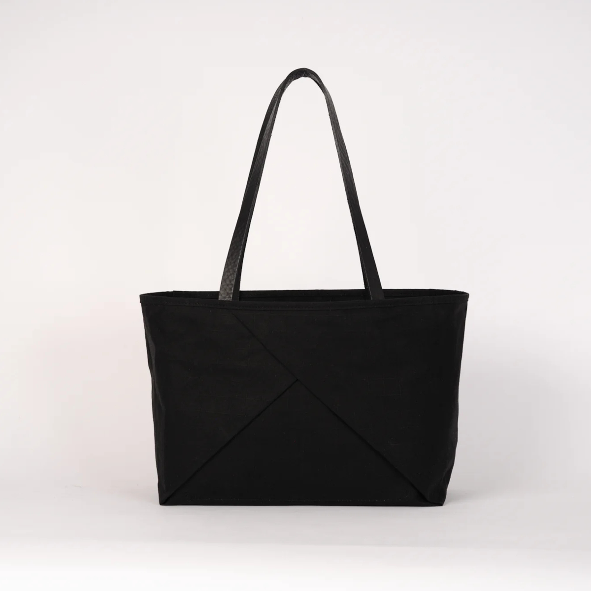 A black canvas tote bag with black shoulder straps, featuring a diagonal crisscross design on the front, set against a plain light gray background.