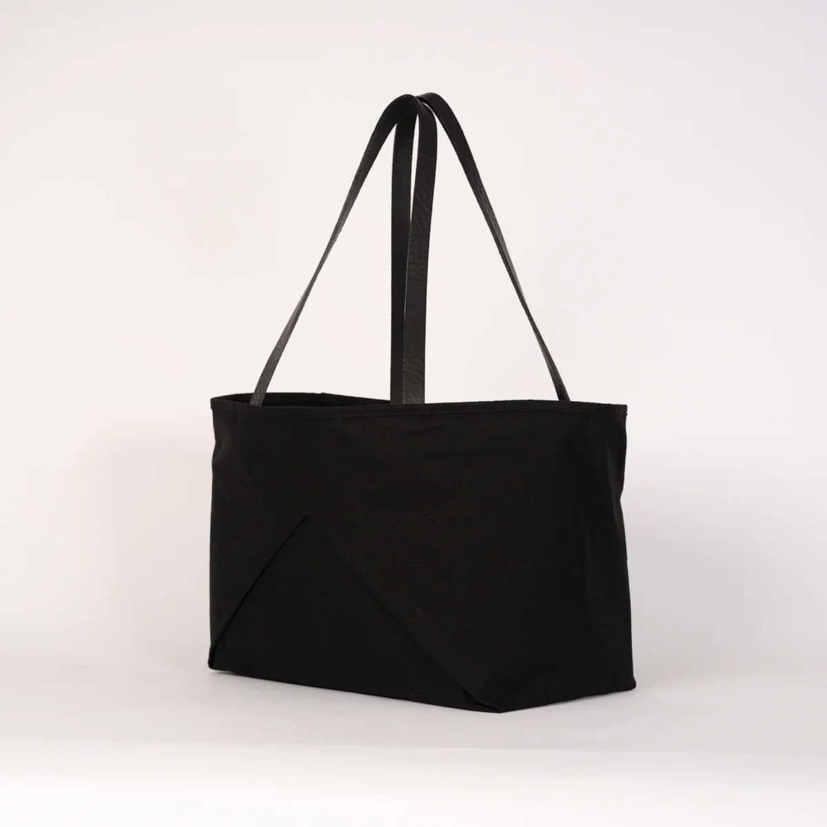 A black canvas tote bag with two long shoulder straps, photographed against a plain white studio background.