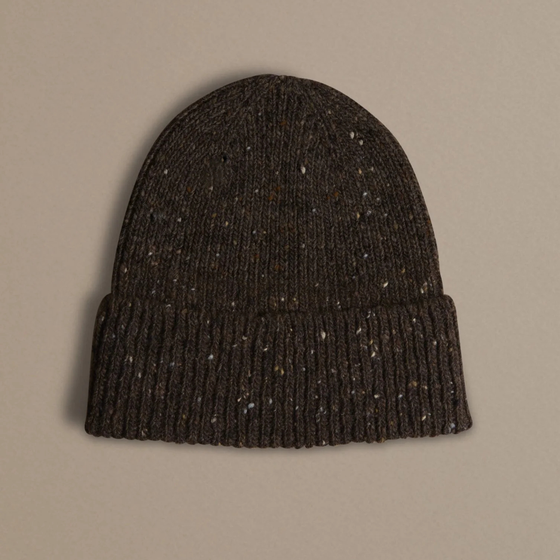 A dark brown knit beanie hat with subtle multicolor flecks, shown flat against a solid beige background.