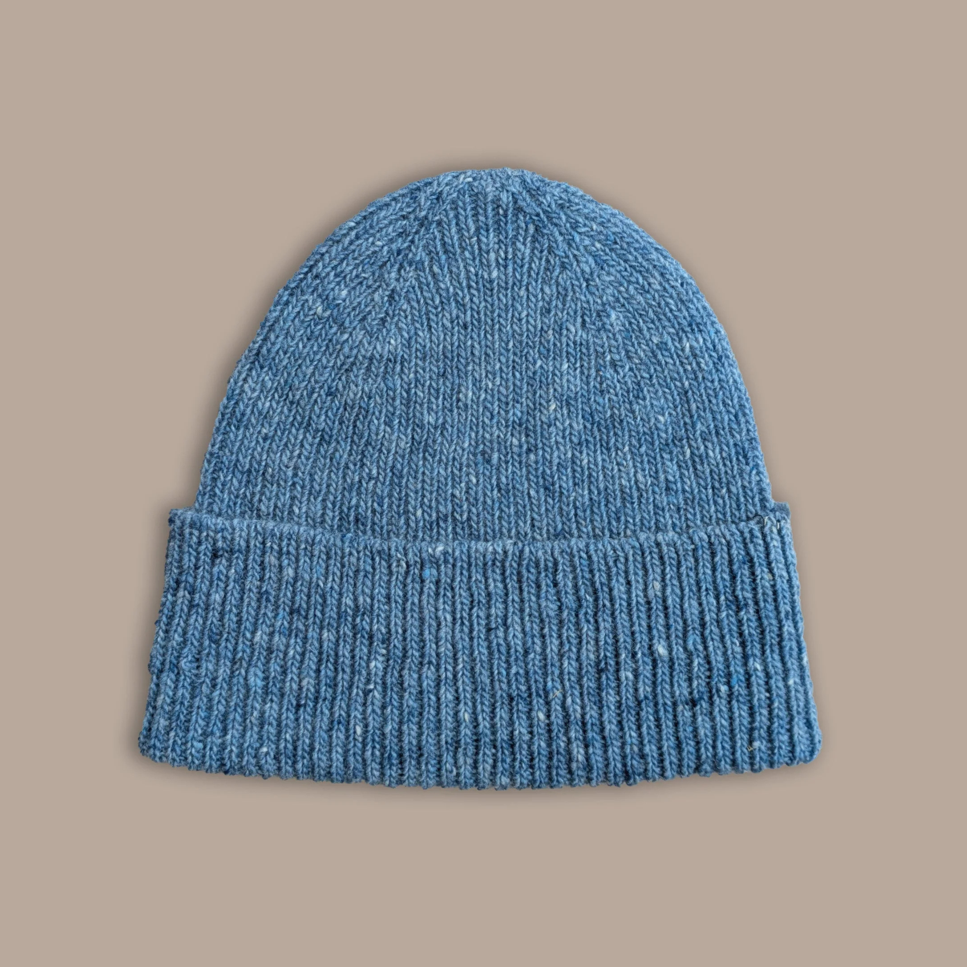 A heathered blue knit beanie hat with a folded cuff, shown flat against a solid taupe background.