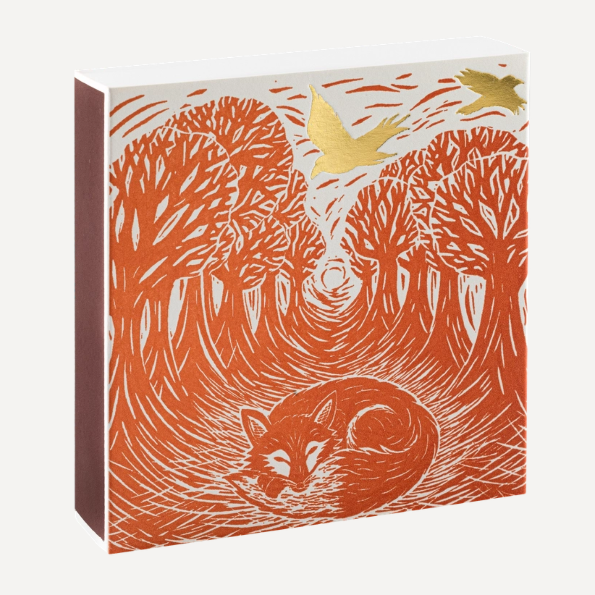 A square art print or book cover featuring an orange linocut-style forest scene with a sleeping fox at the bottom, two flying birds at the top, and a small gold foil accent. The product is shown at a slight angle against a light gray background.