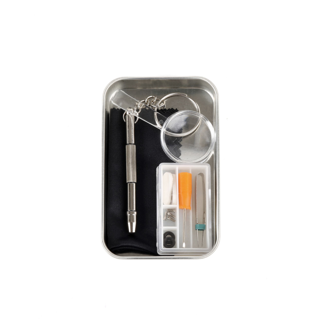 Eyeglass repair kit in a metal tin. Includes screwdriver, magnifying glass, cleaning cloth, and small parts.