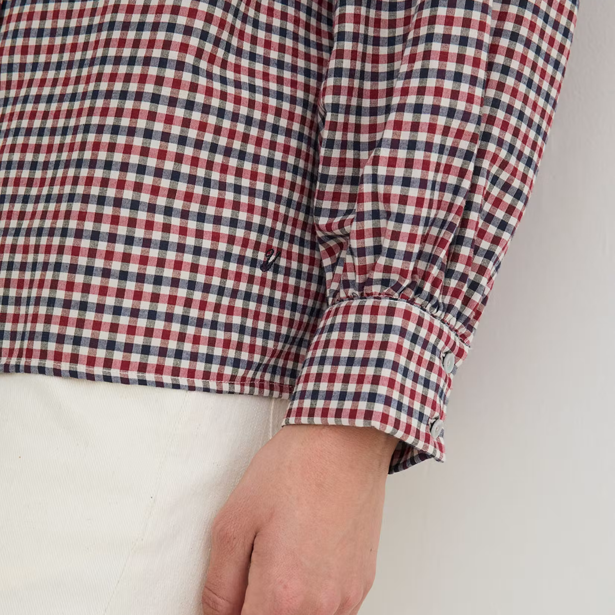 Close-up of a person wearing a red, navy, and white gingham long-sleeve shirt with a gathered cuff, paired with white pants.