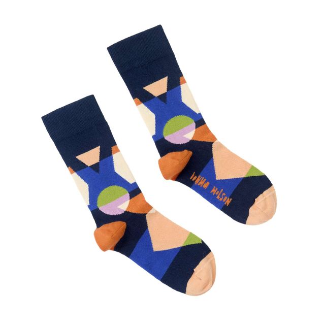 A pair of crew socks with a colorful geometric pattern on a solid white background. The socks feature a navy blue cuff, blue and beige abstract shapes, orange accents, and a green circle, with the brand name 'JANE WILSON' printed in orange on the sole of one sock.