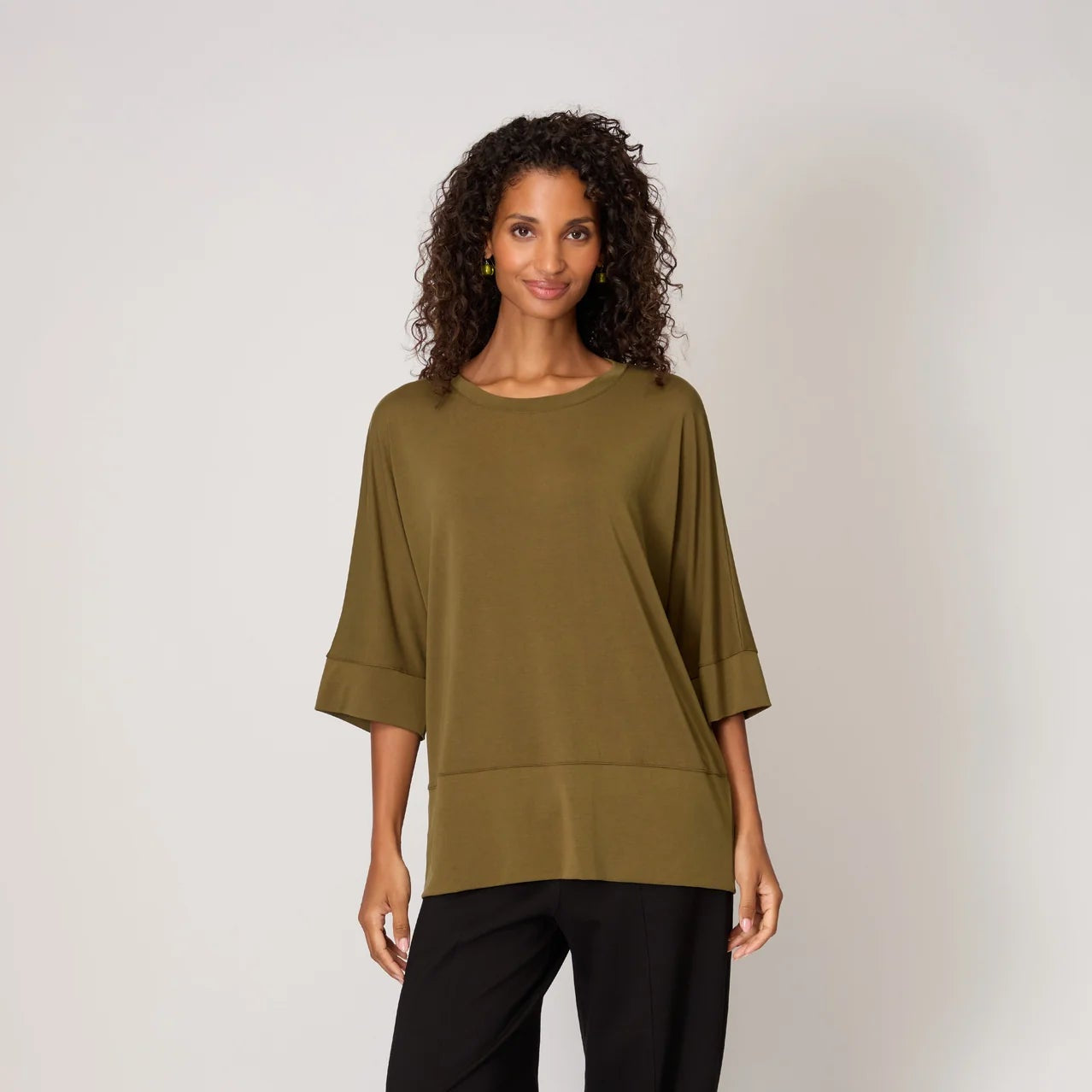 Woman wearing an olive green top and black pants on a white background
