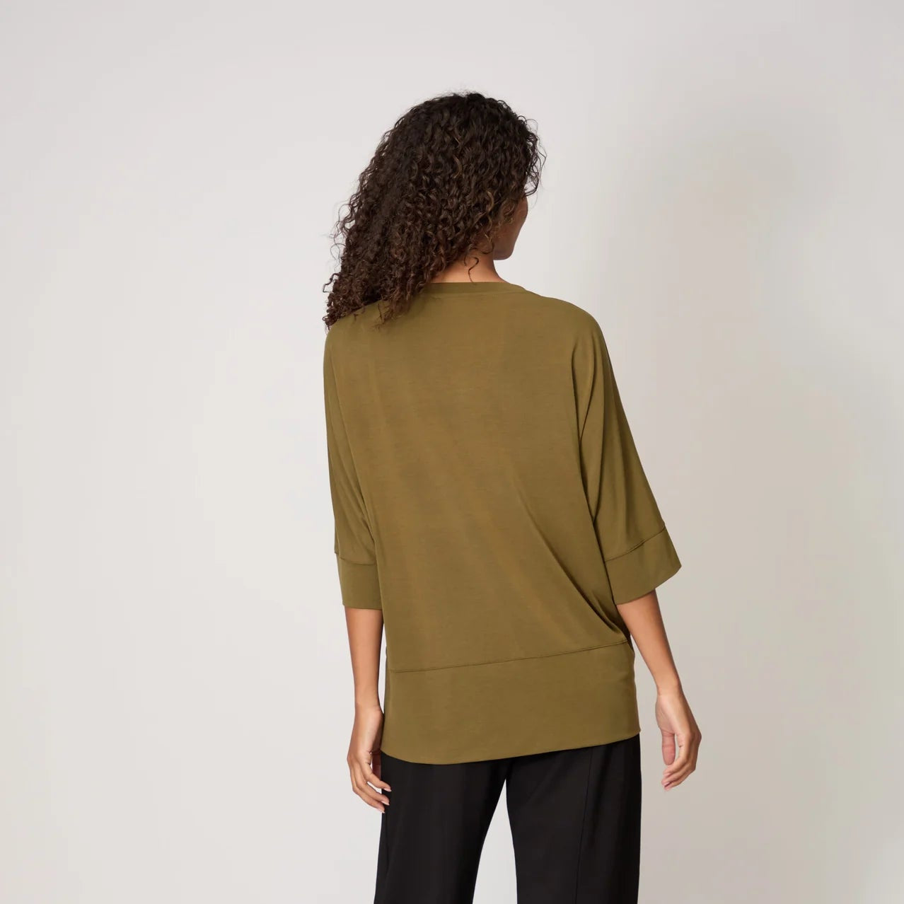 Person wearing a green sweater and black pants on a white background