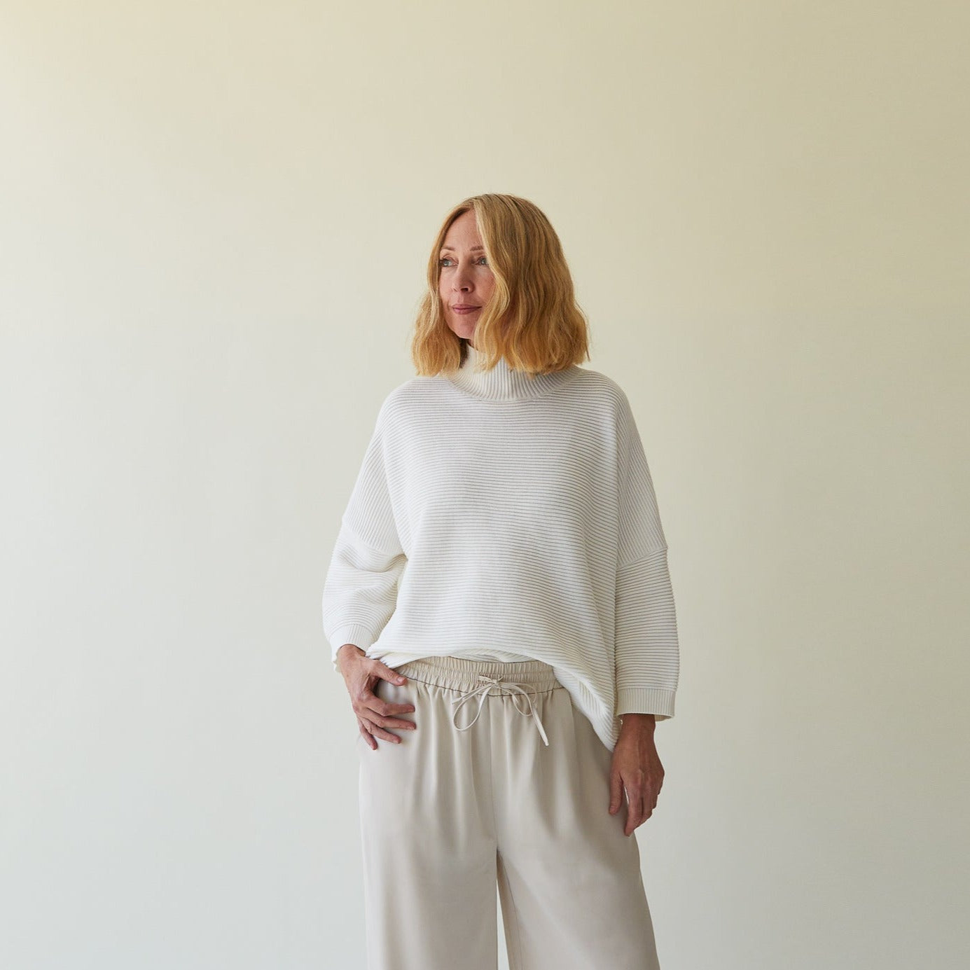 White ribbed knit turtleneck sweater with relaxed fit and three-quarter sleeves.