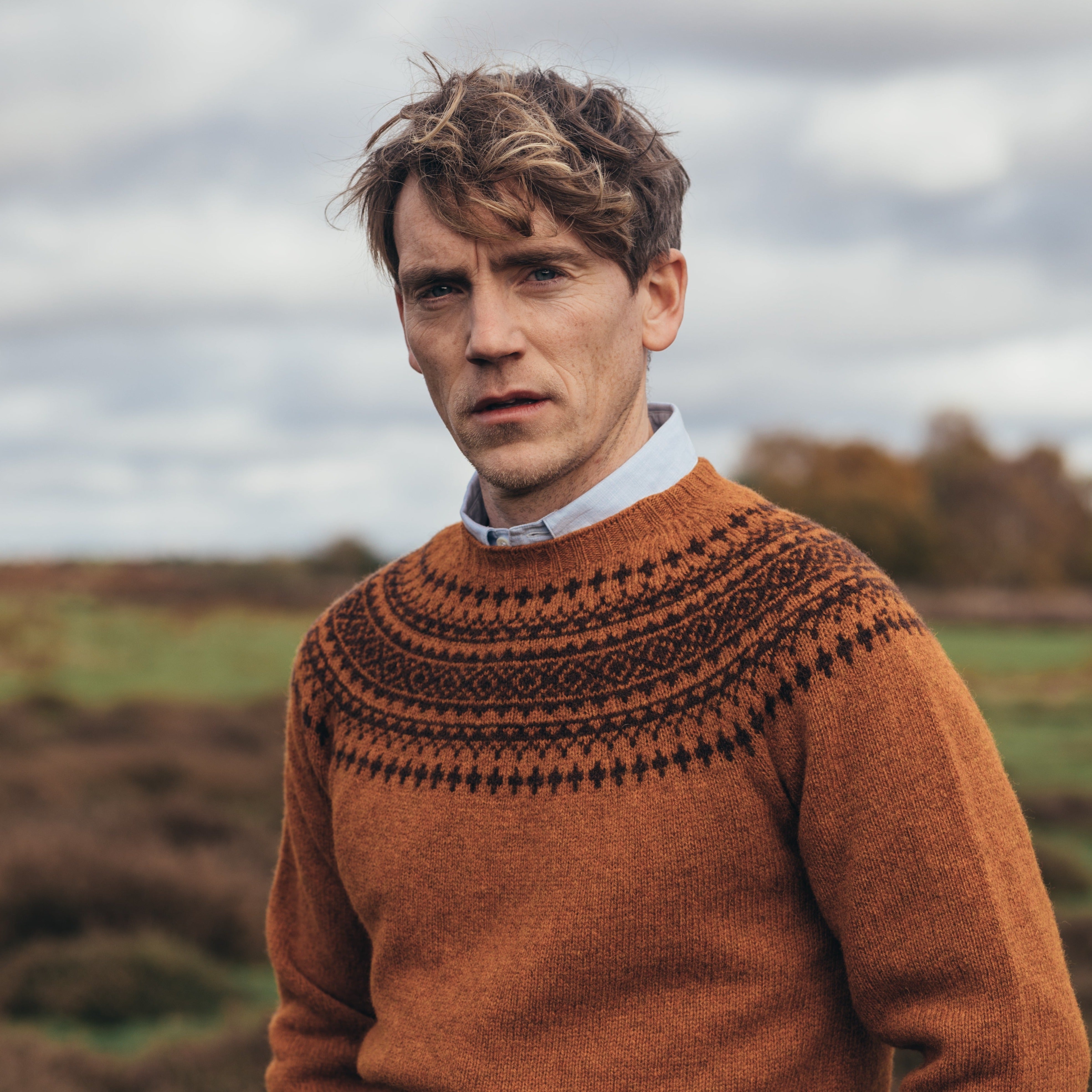 A rust-colored crewneck sweater with a dark brown Fair Isle yoke pattern. The sweater is knit from a soft-looking yarn.