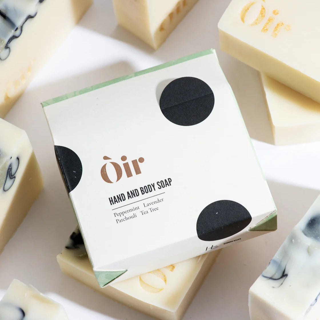 A bar of hand and body soap with peppermint, lavender, patchouli, and tea tree scents from Oir surrounded by other similar bars with a visible brand name and logo on the packaging.