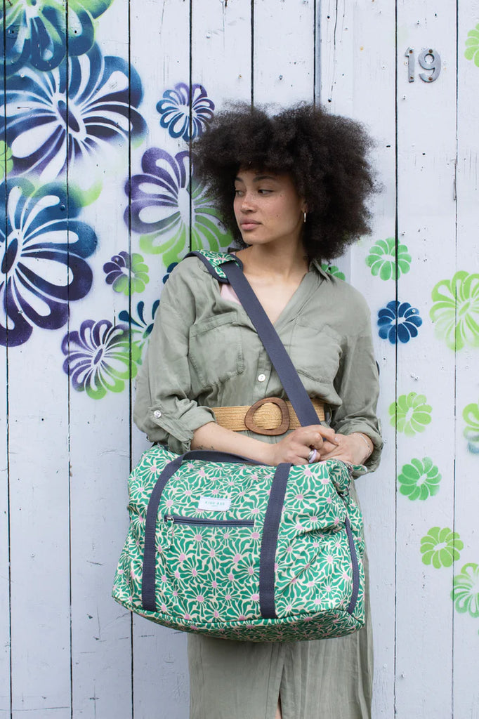 Green floral-print duffel bag with dark gray straps, carried by a person.