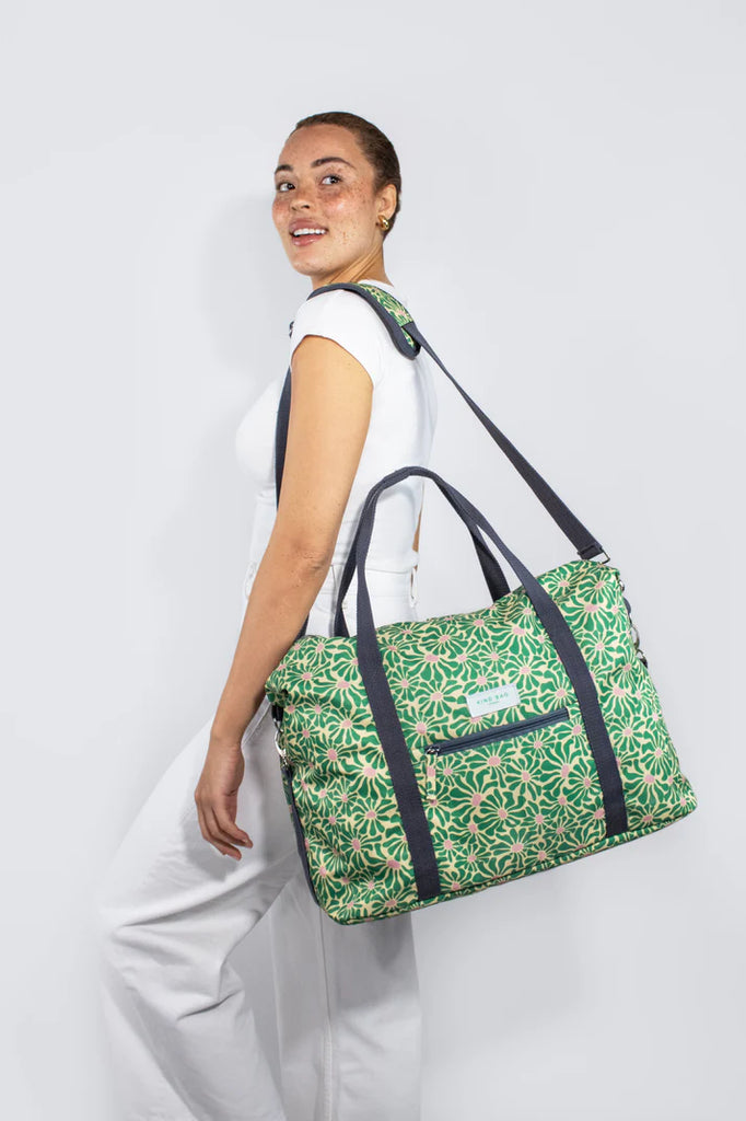 Green floral-print duffel bag with dark gray straps and handles.  A small zippered pocket is visible on the front.