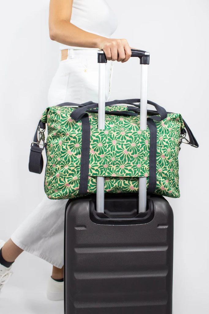 Green floral-print duffel bag sitting atop a black rolling suitcase.