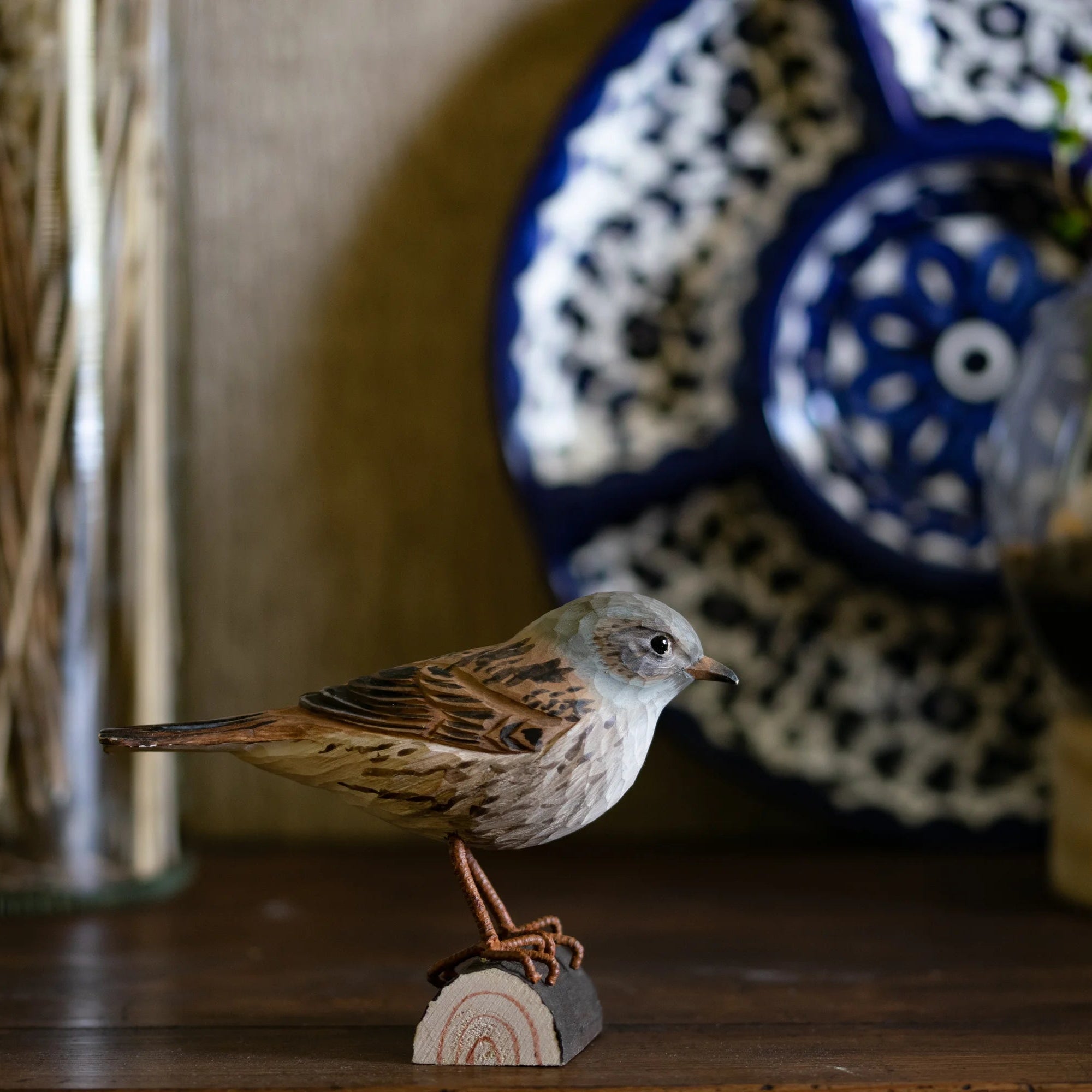 Small bird perched on a wooden block with decorative plates and plants in the background