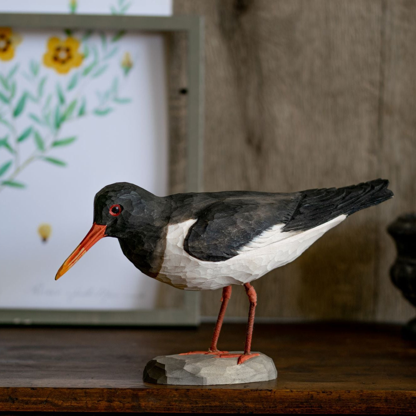 Model of a bird on a wooden surface with a framed picture in the background