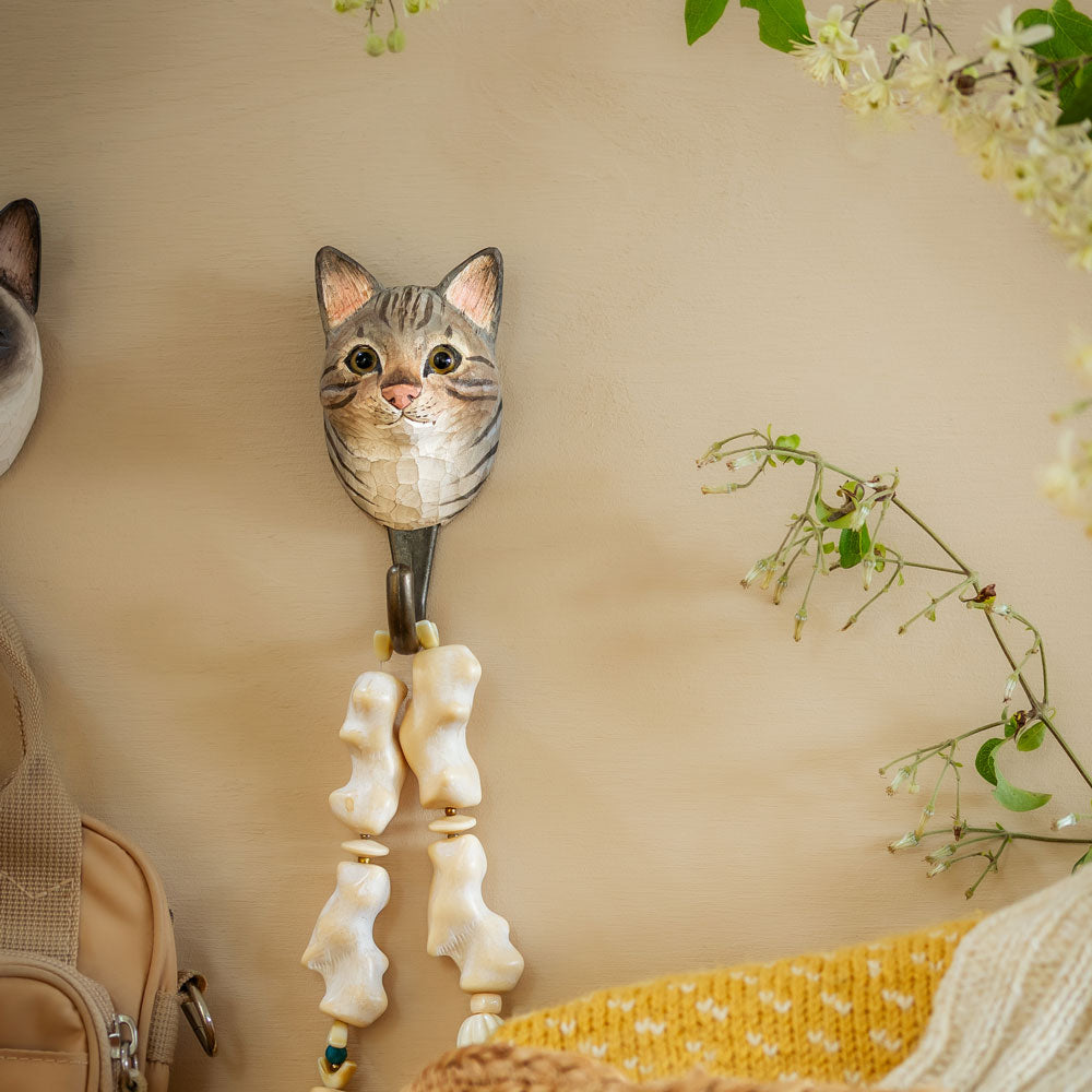 Cat-shaped wall hook with decorative elements on a beige wall.