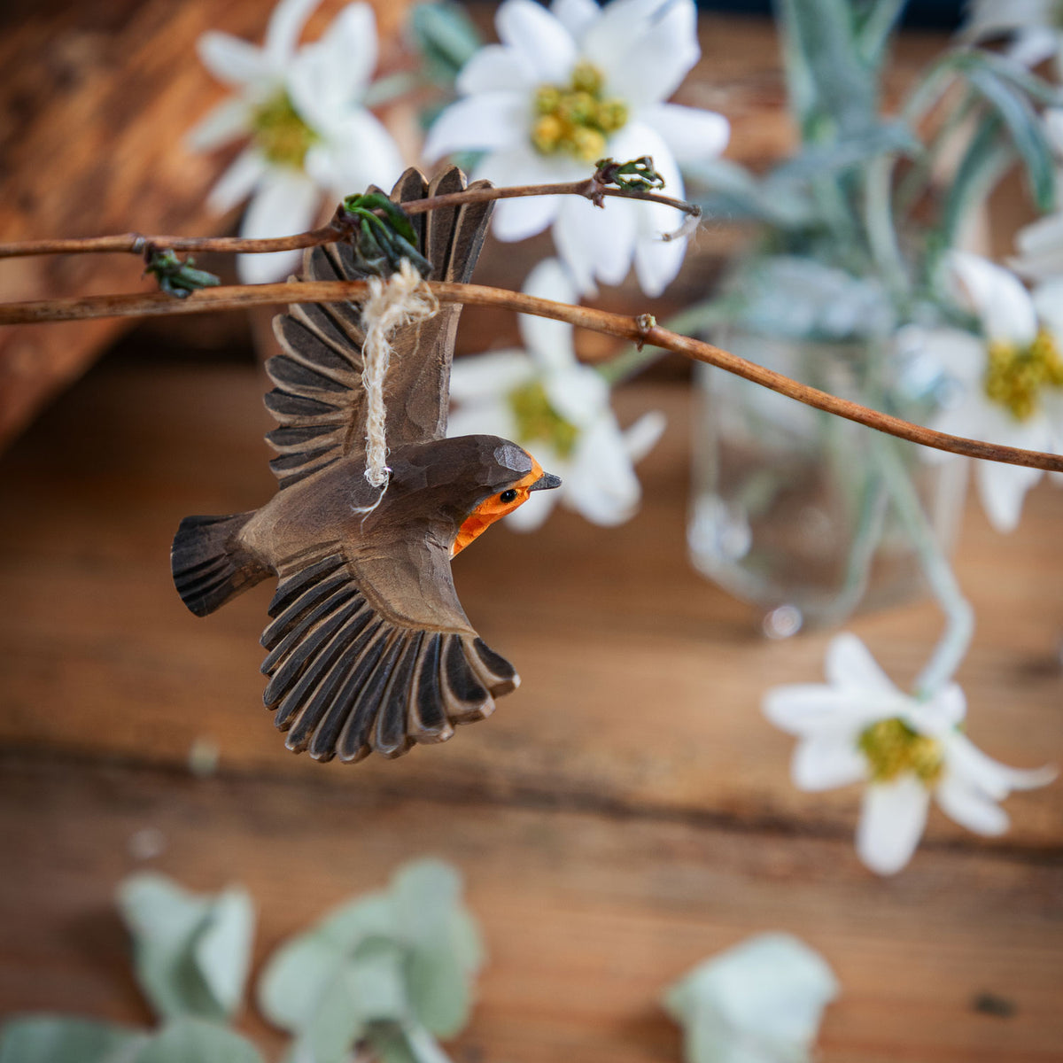 Decorative bird ornament hanging on a branch with flowers and plants in the background