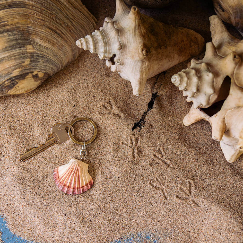 Keychain with a shell pendant on sand surrounded by seashells