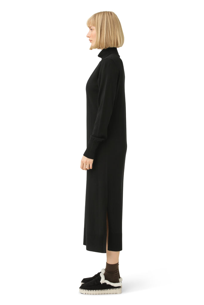 Profile view of a woman wearing a black midi turtleneck dress with a side slit, and dark brown socks with black platform mules