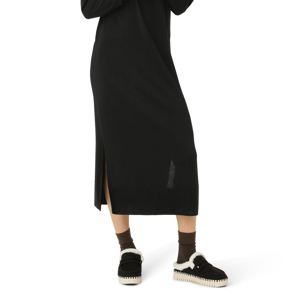 Woman wearing black midi dress and black suede loafers with cream shearling trim and cream platform sole.