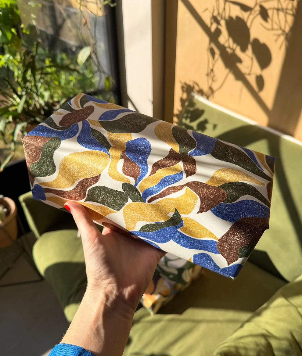 Hand holding a colorful patterned pouch outdoors with greenery in the background
