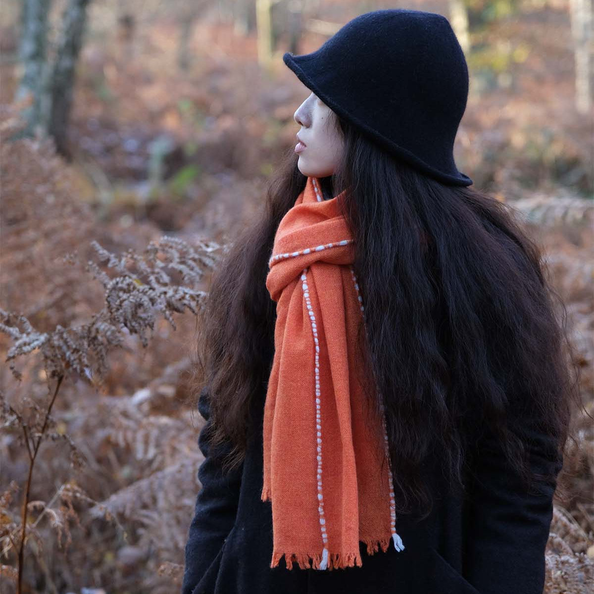 Person wearing a black hat and orange scarf standing in a forest with frosty ground.