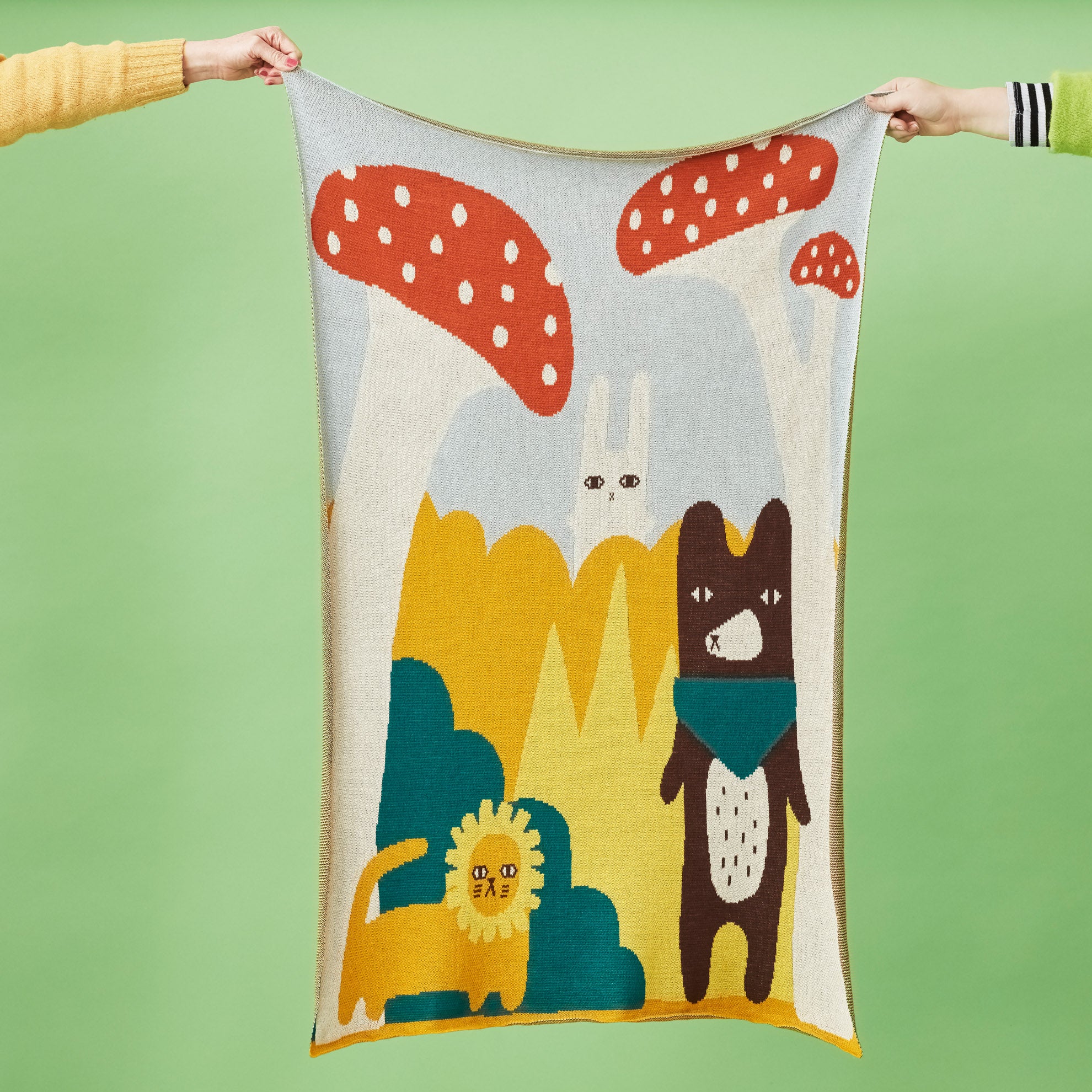 A colorful Donna Wilson blanket featuring a lion, rabbit, and bear against blue and yellow backgrounds with red mushrooms.