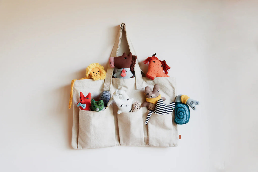 A cream bag from Donna Wilson holds colorful plush animals: orange horse, yellow lion, red fox, and green alligator.