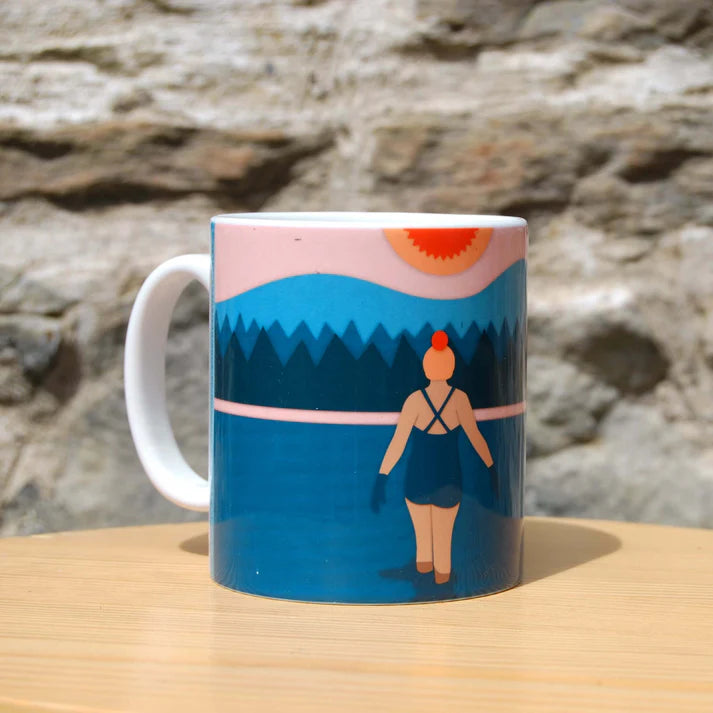 Mug featuring a stylized illustration of a woman in a bathing suit, standing by a lake at sunset, against a backdrop of