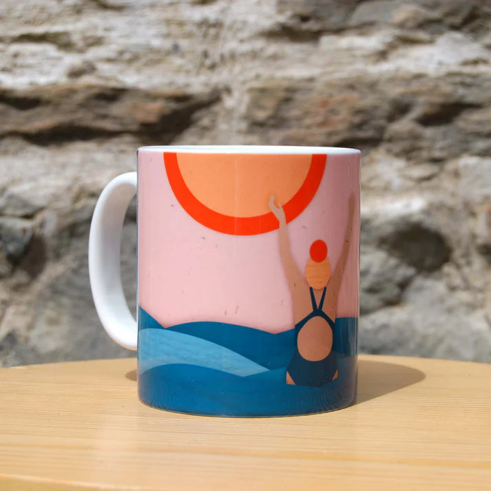 Mug featuring illustration of swimmer in ocean with setting sun.  Pink, orange, and teal color palette.