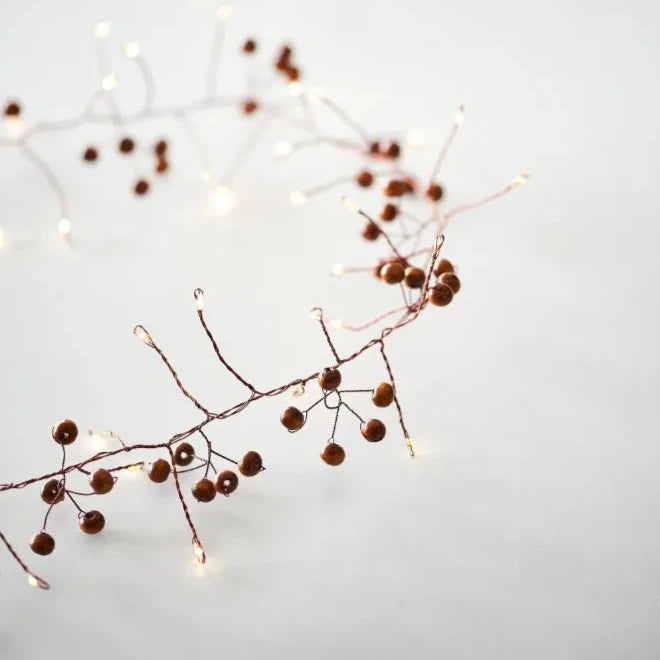 Copper wire string lights adorned with brown wooden beads. Warm white LED lights illuminate the garland.