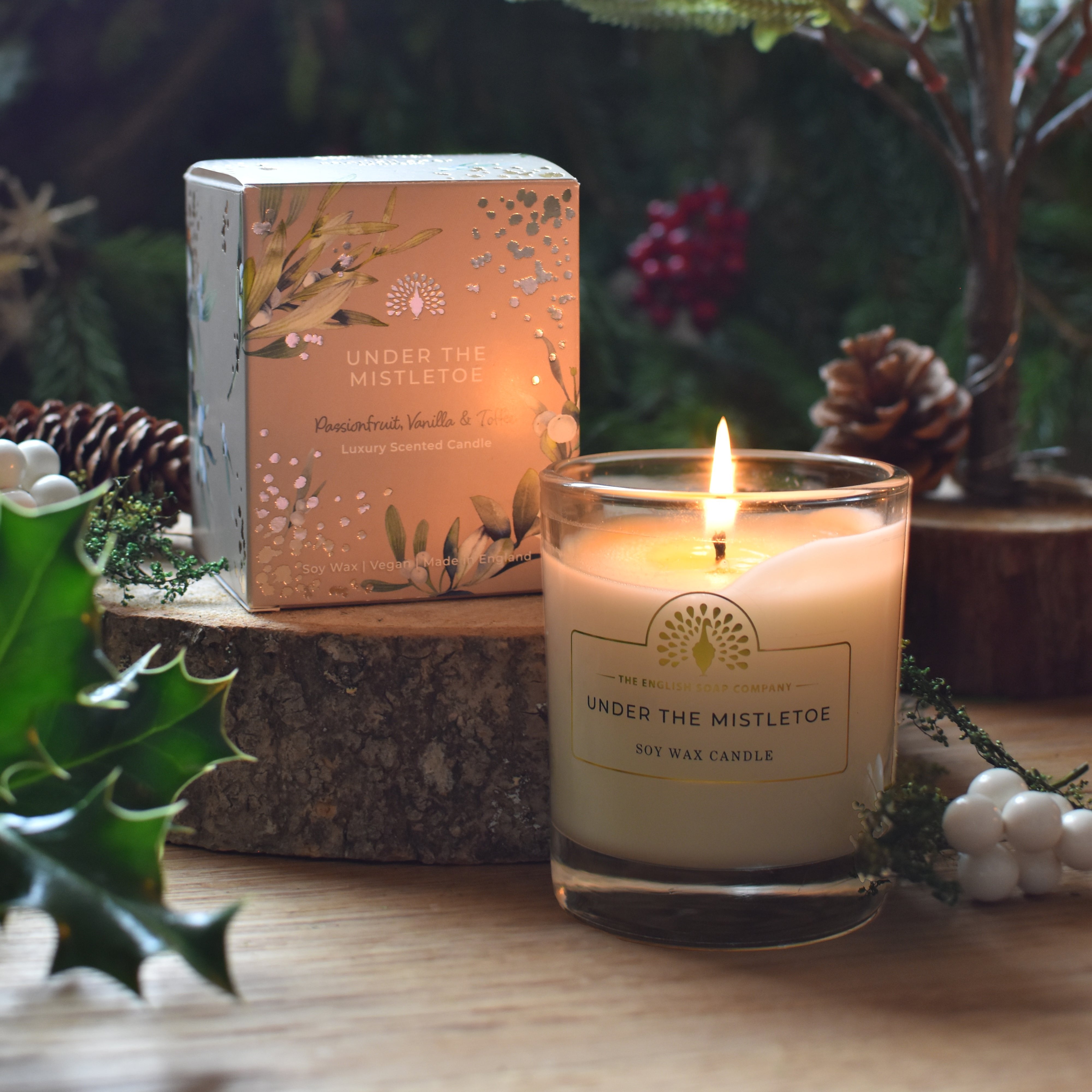 Lit soy candle in a clear glass jar;  "Under the Mistletoe" label;  passionfruit, vanilla & toffee scent.