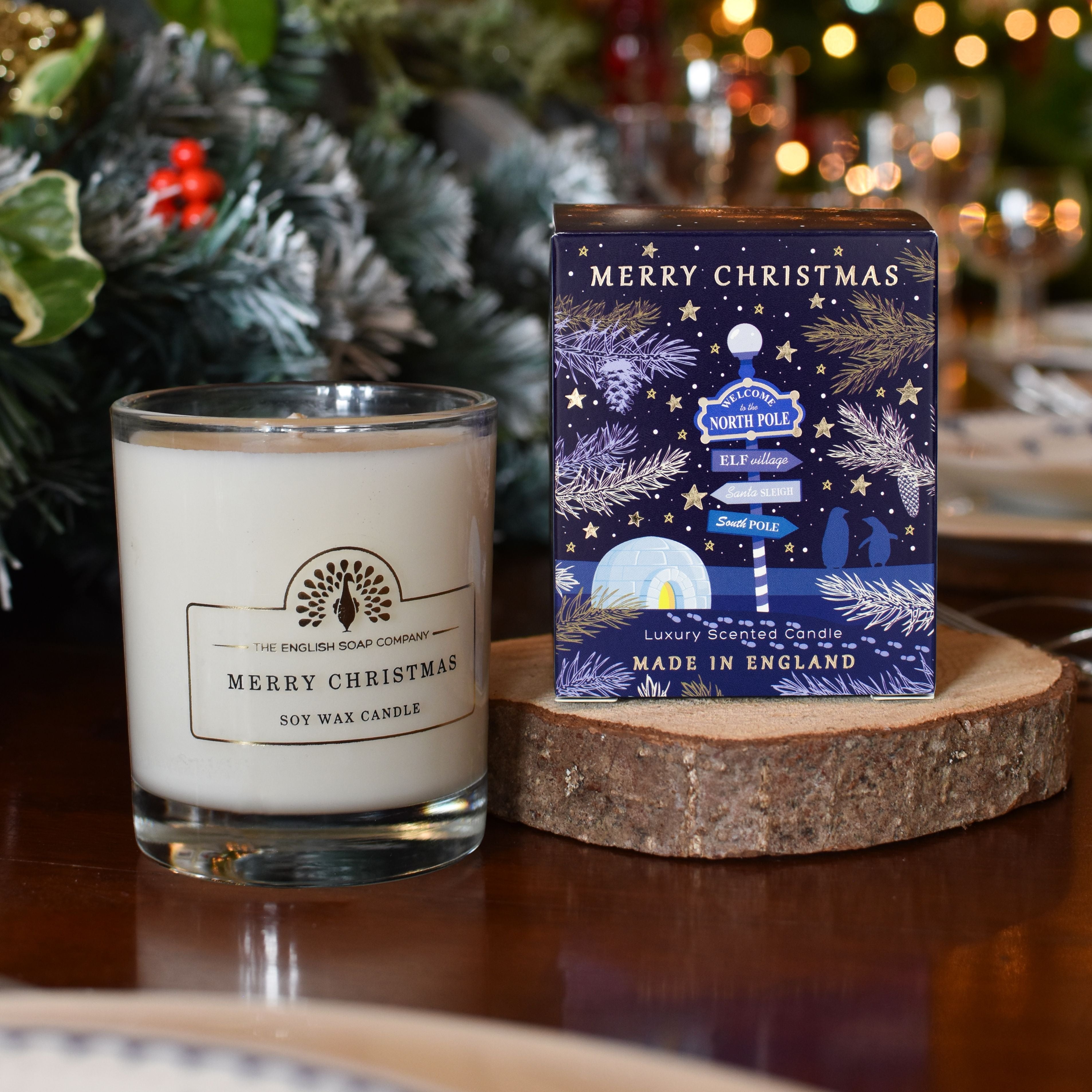 Soy wax candle in a clear glass jar, labeled "Merry Christmas," next to its matching gift box featuring a North Pole elf