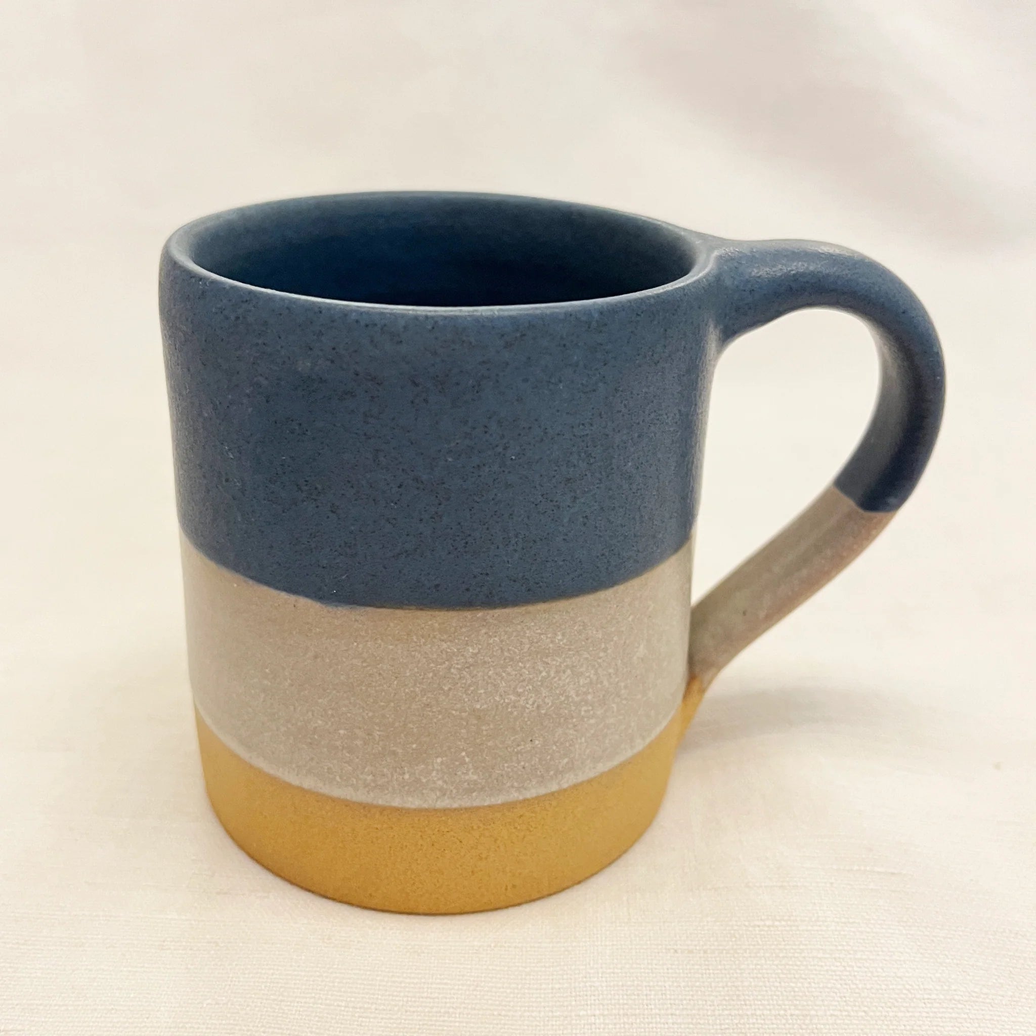 Stoneware mug with a dark blue top, a light grey middle band, and a mustard yellow bottom.