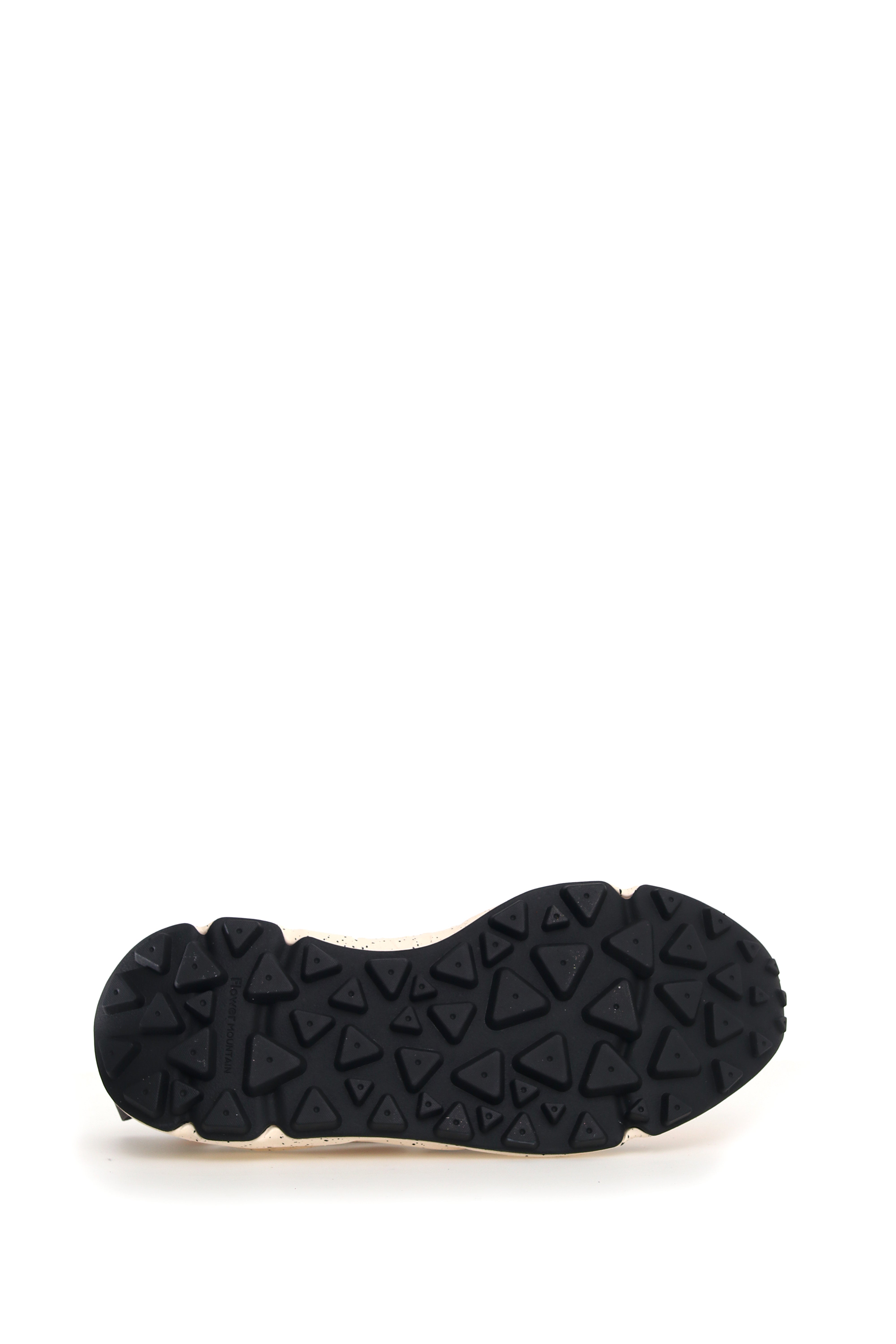 Close-up of a shoe's sole, featuring a cream-colored base and a black, textured tread with triangular and circular patterns.