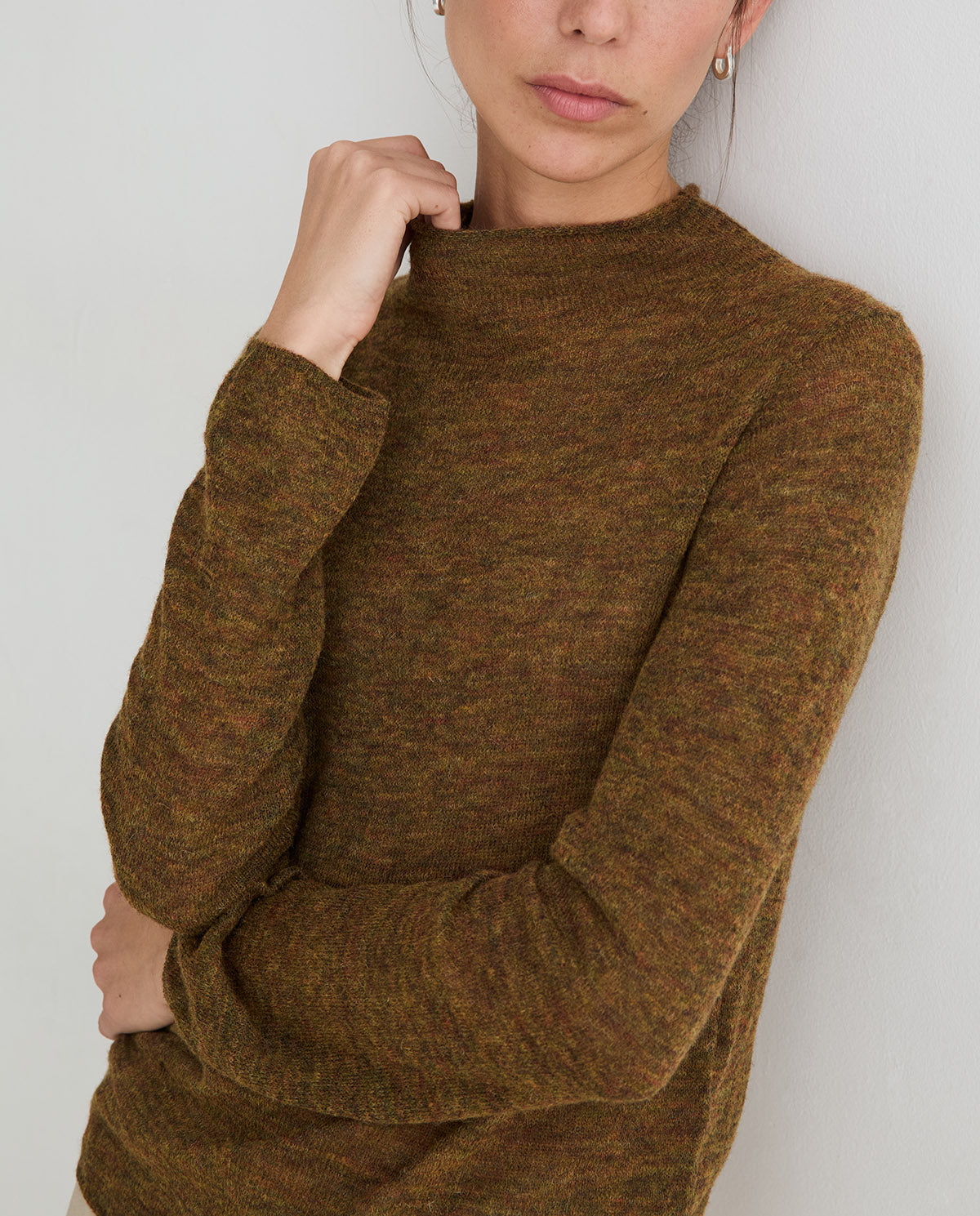 A close-up of a woman wearing a textured, heathered brown knit mock neck sweater against a plain light gray background.