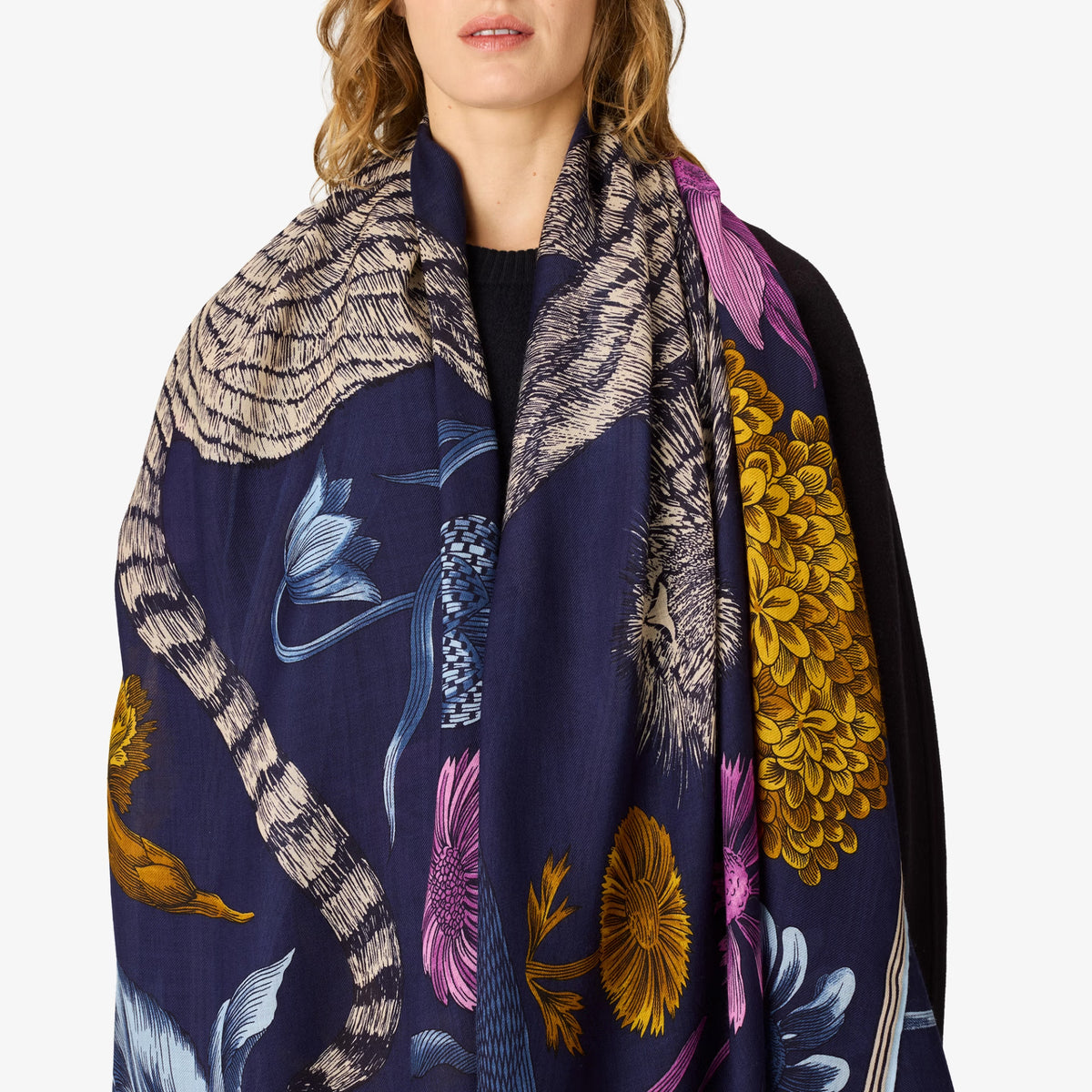 A navy blue scarf with a detailed print of a cat's body, floral elements, and abstract patterns, worn by a model against a plain white background.
