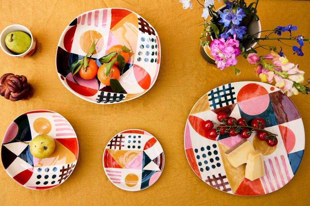 Colorful ceramic plates with geometric patterns on a yellow surface, accompanied by small bowls and flowers.